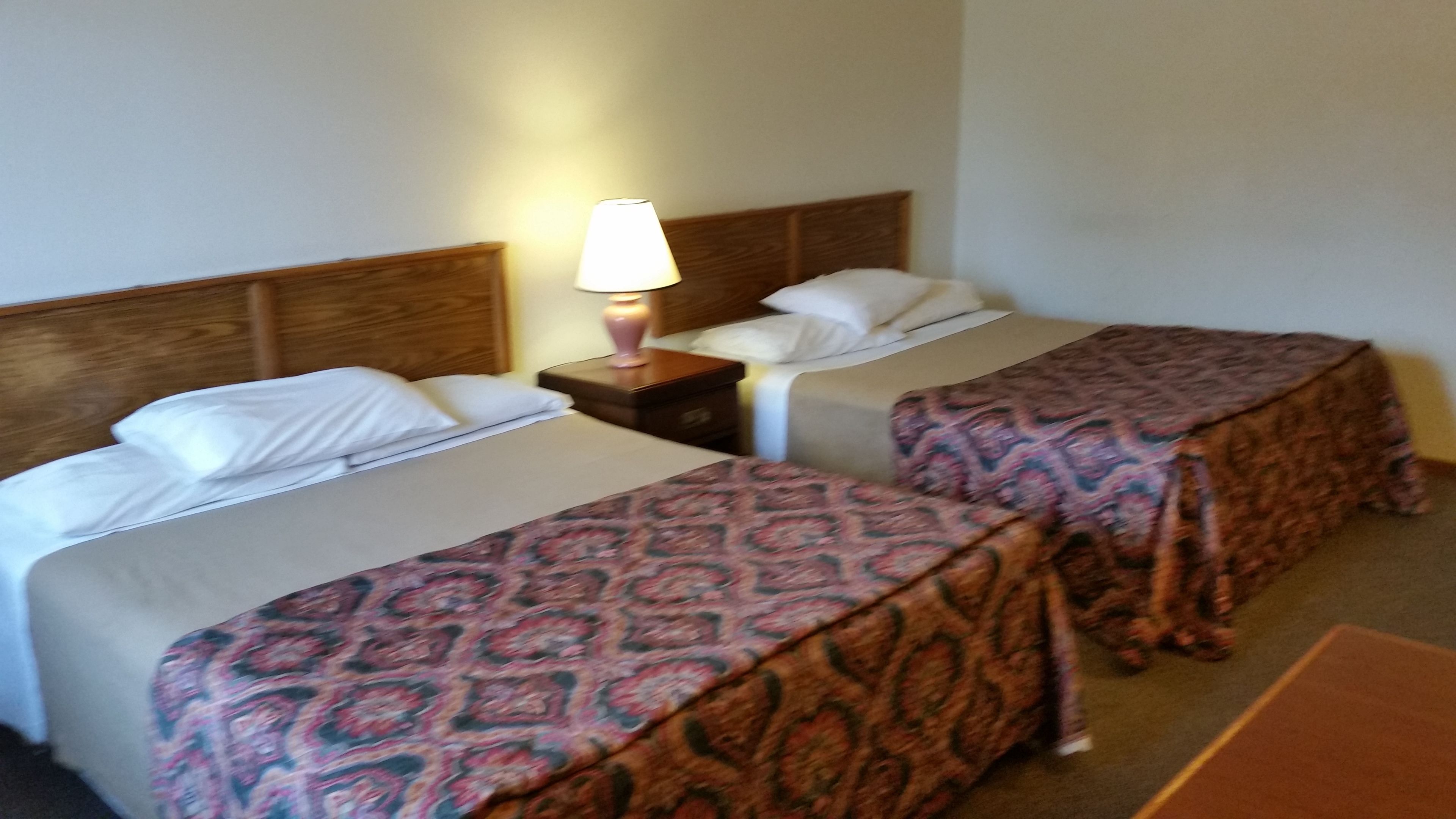 A hotel room with two beds, each with a patterned bedspread, a nightstand with a lamp, and a wooden headboard.