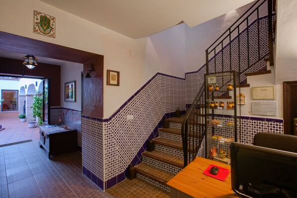 A staircase with patterned tiles, a wooden desk with a computer, and a view of the outside. - Al-mudawar (Almodovar del Rio)