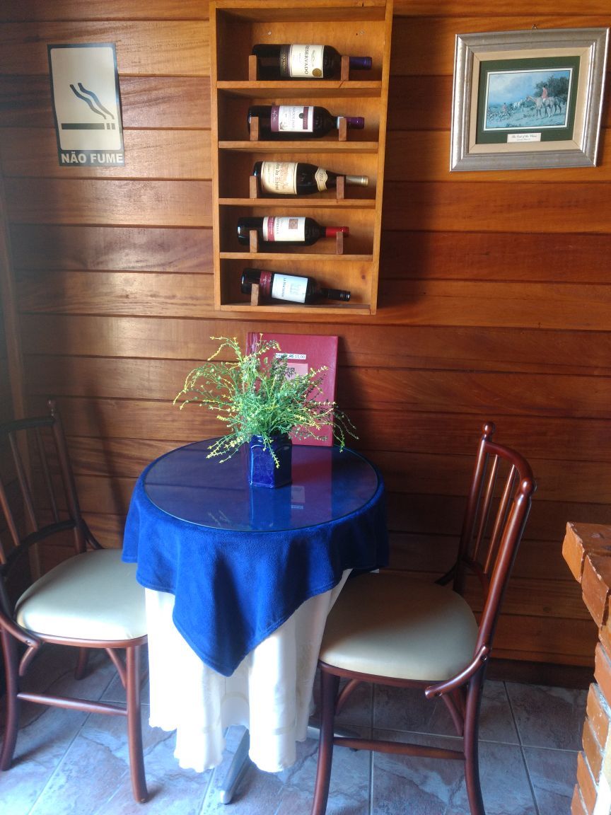 Un interior de madera con una mesa redonda, dos sillas, un mantel azul, una planta pequeña y una estantería para botellas de vino.