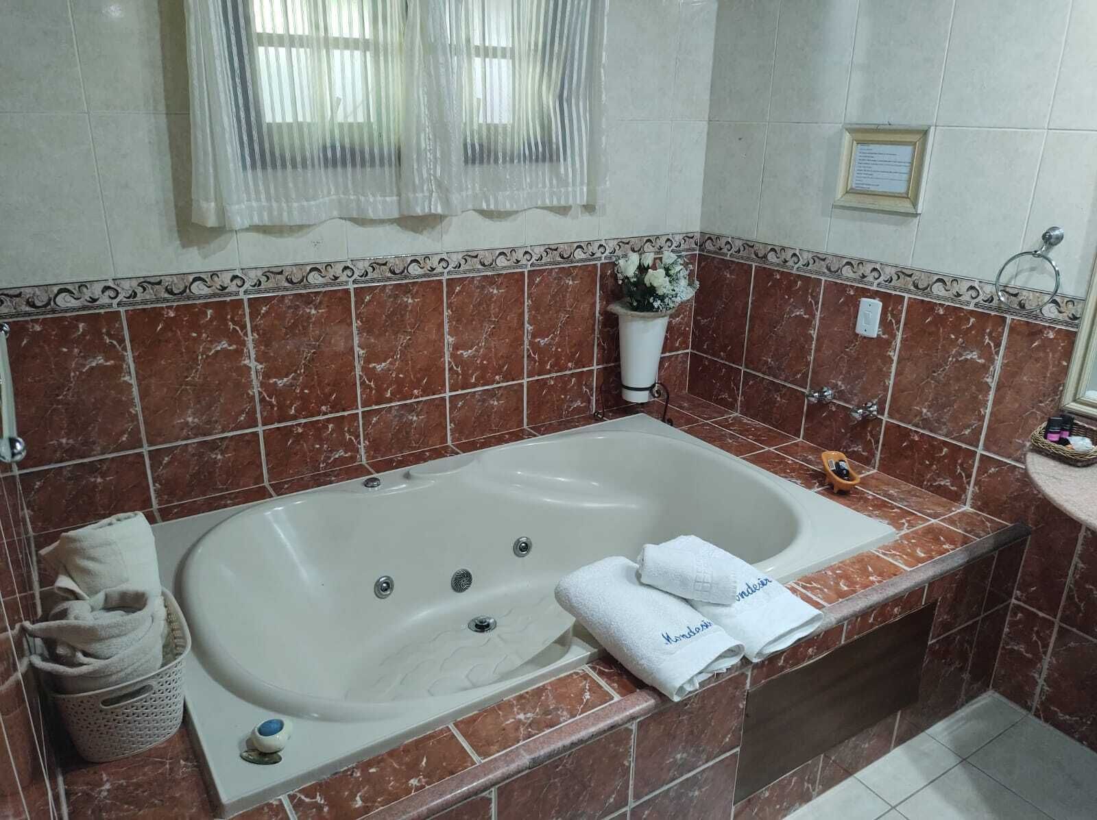 A bathroom with a large bathtub, a shower area, and a vanity with a mirror. There are towels and toiletries on the vanity.