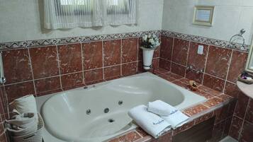 A bathroom with a large bathtub, a shower area, and a vanity with a mirror. There are towels and toiletries on the vanity.