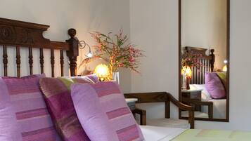 A neatly made bed with purple pillows, a bedside lamp, and a mirror reflecting the room's decor.