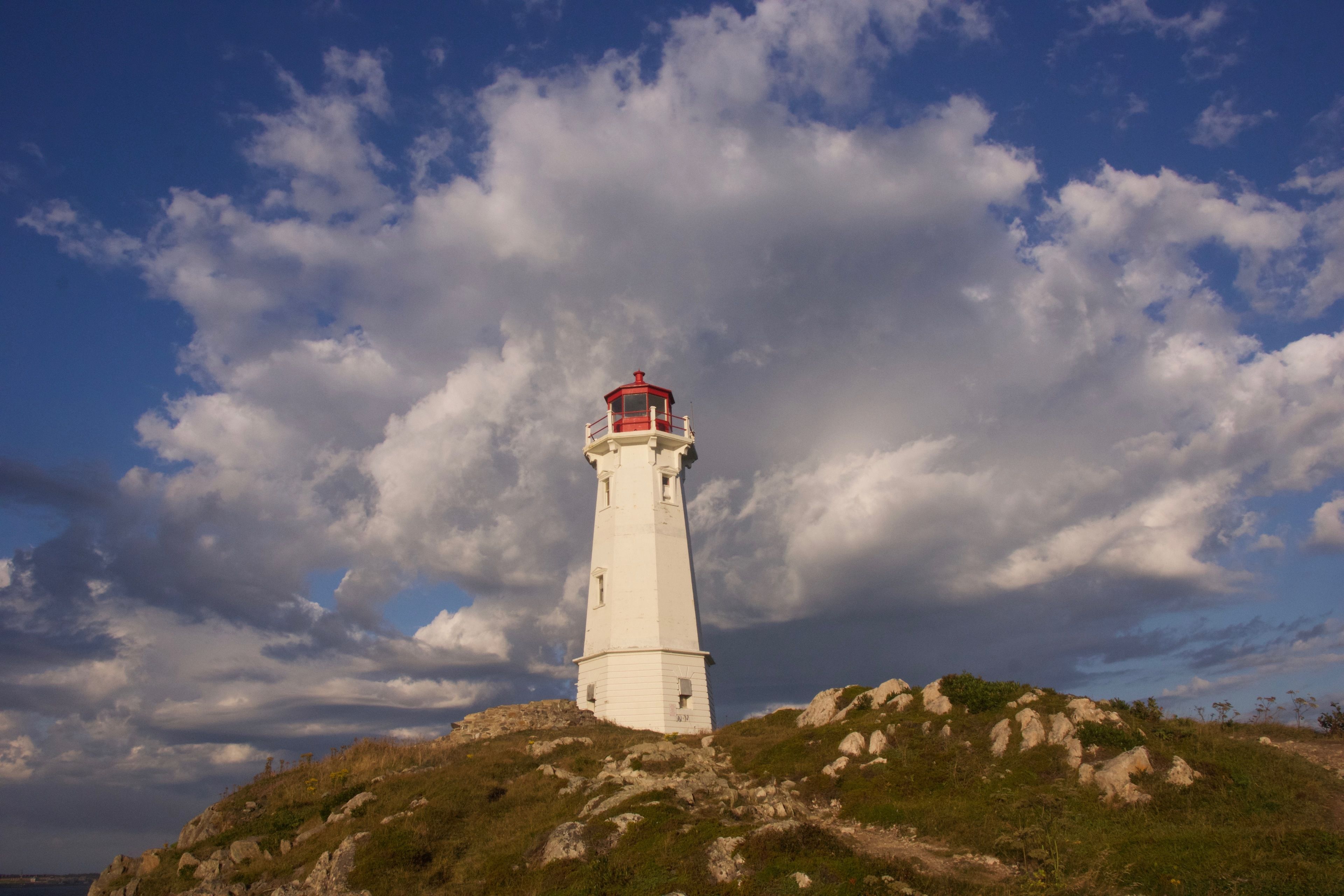 Un faro en una colina rocosa con cielo despejado y nubes.