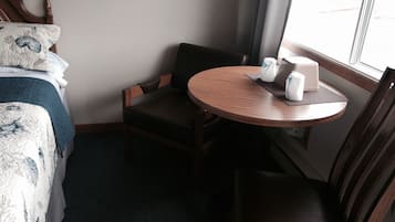 Habitación de hotel con cama, una silla, una mesita y una ventana.