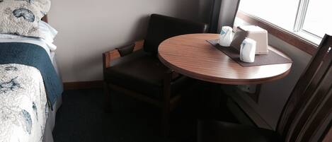 Habitación de hotel con cama, una silla, una mesita y una ventana.