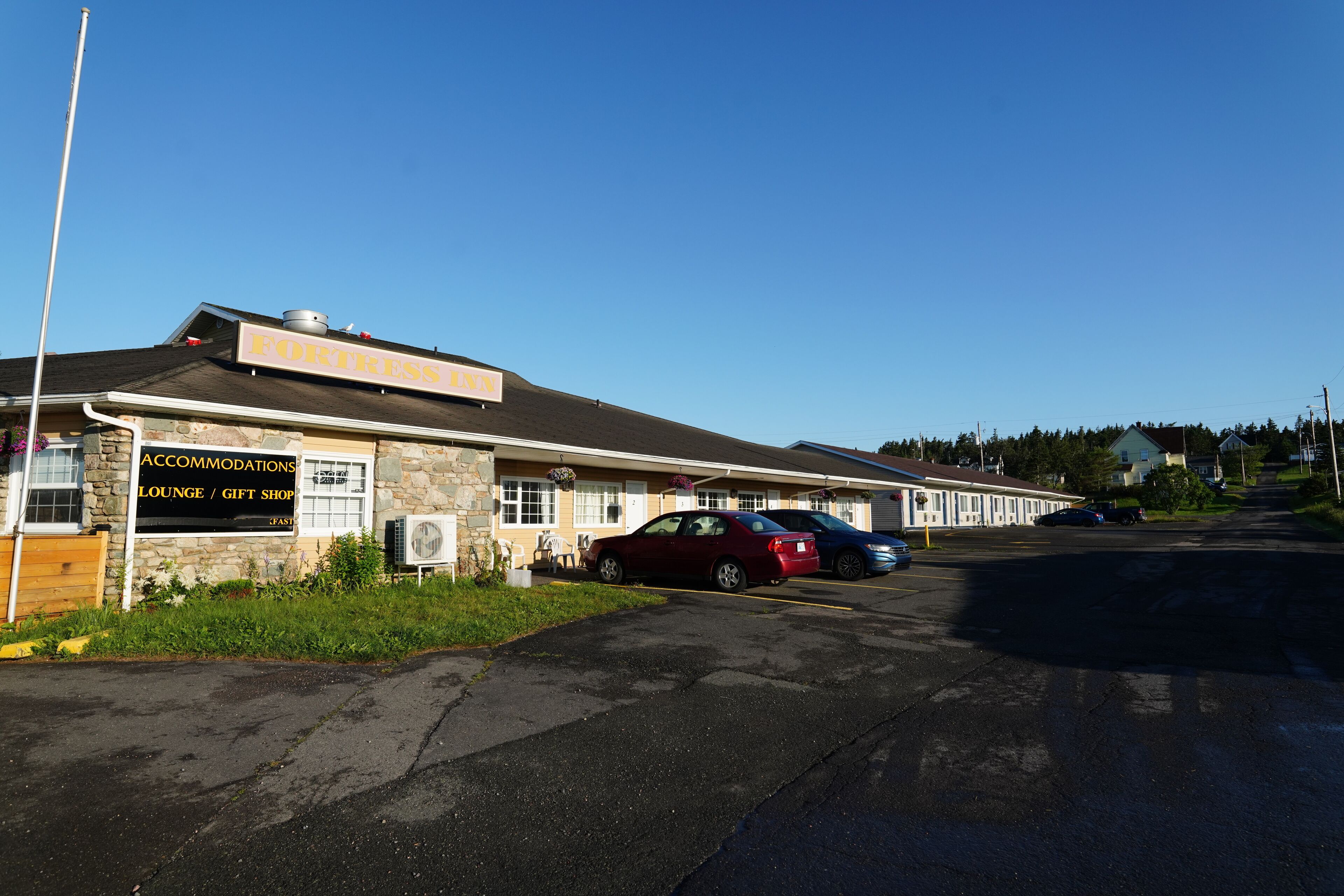 Een gebouw met een bord waarop 'Fortress Inn' en 'Accommodatielounge / Geschenkwinkel' staat. Er staan auto's geparkeerd voor.