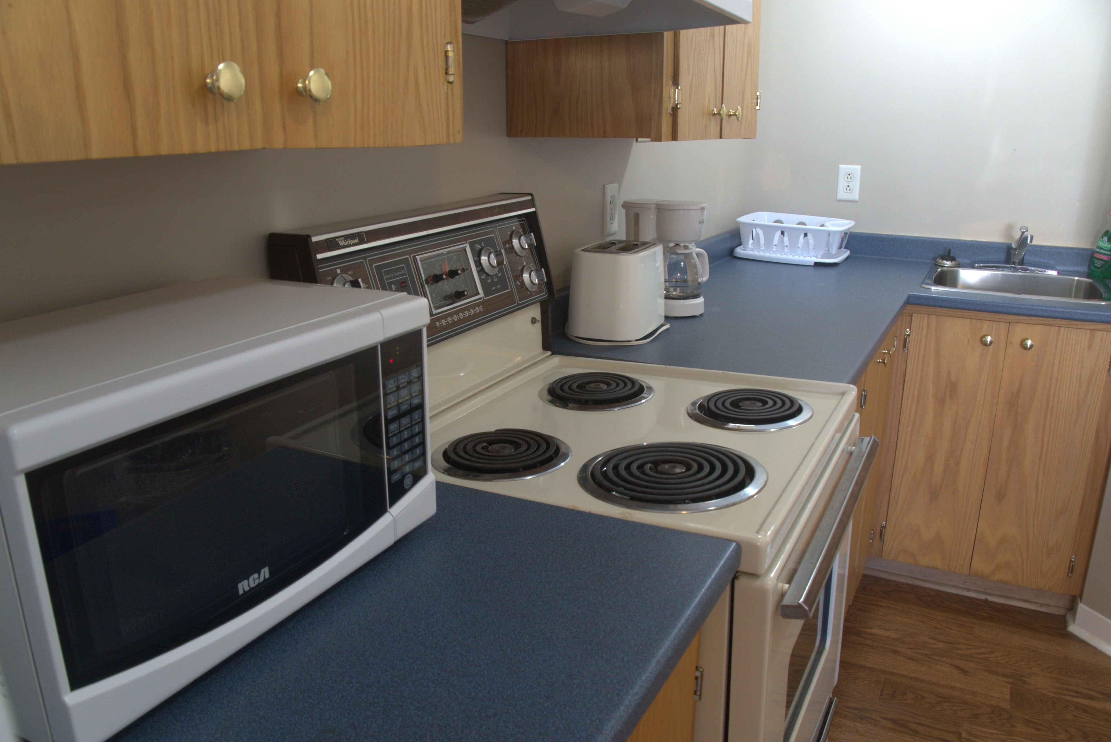 A kitchen with a microwave, stove, coffee maker, and cabinets.
