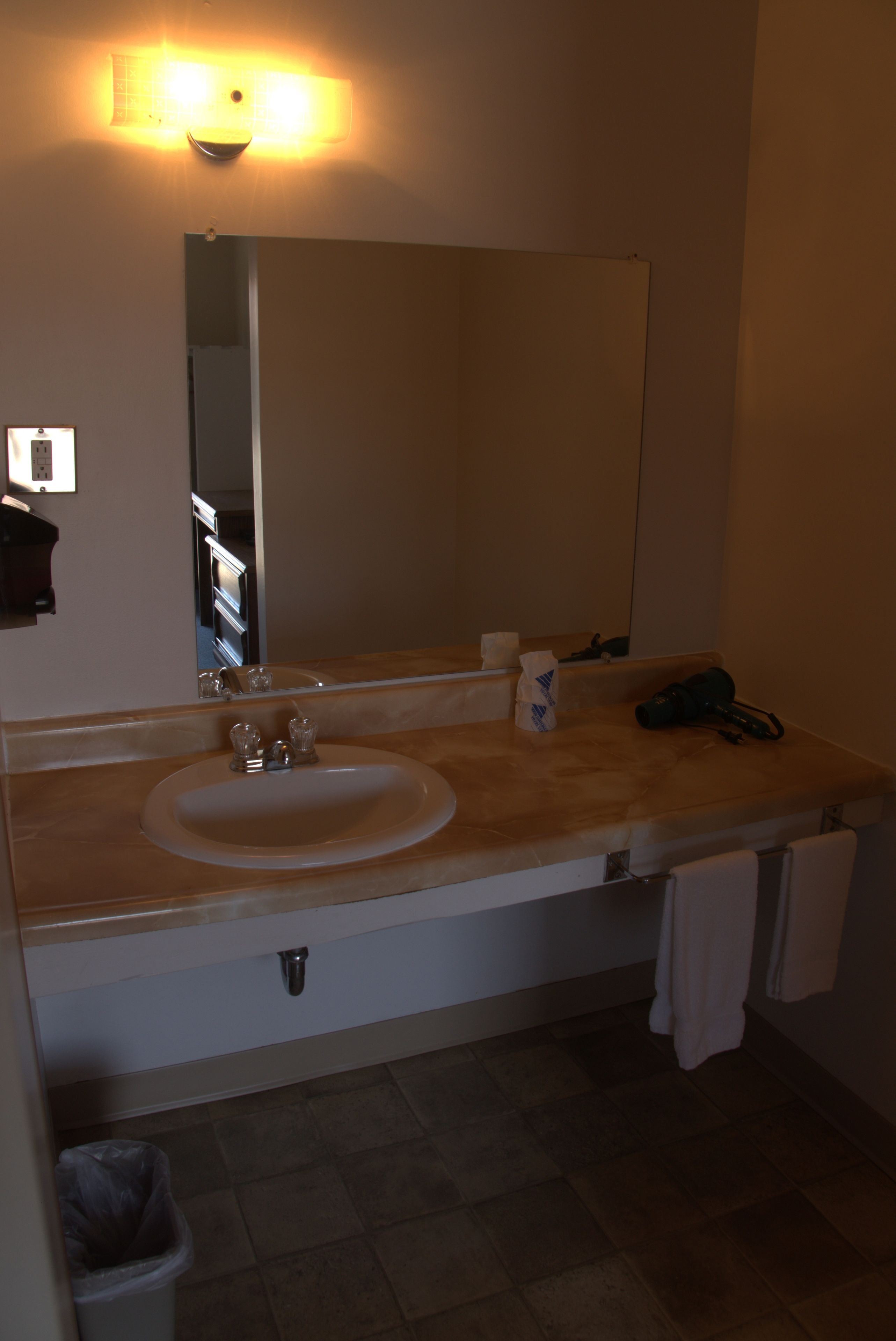 Un baño con lavamanos, espejo, toallero y cubo de basura.