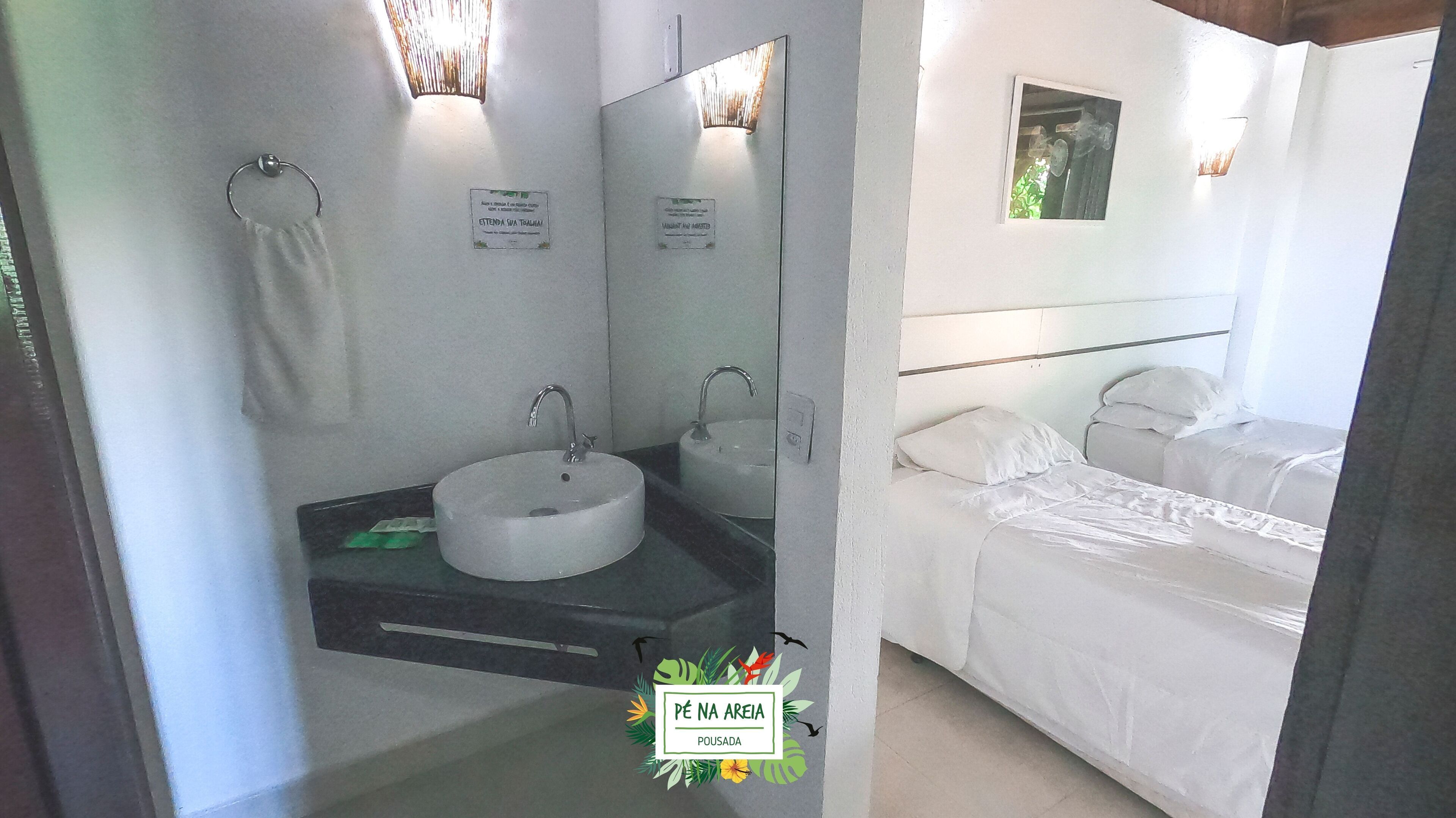 A bathroom with a sink, mirror, and towel rack. There is a bed with white bedding and a pillow.