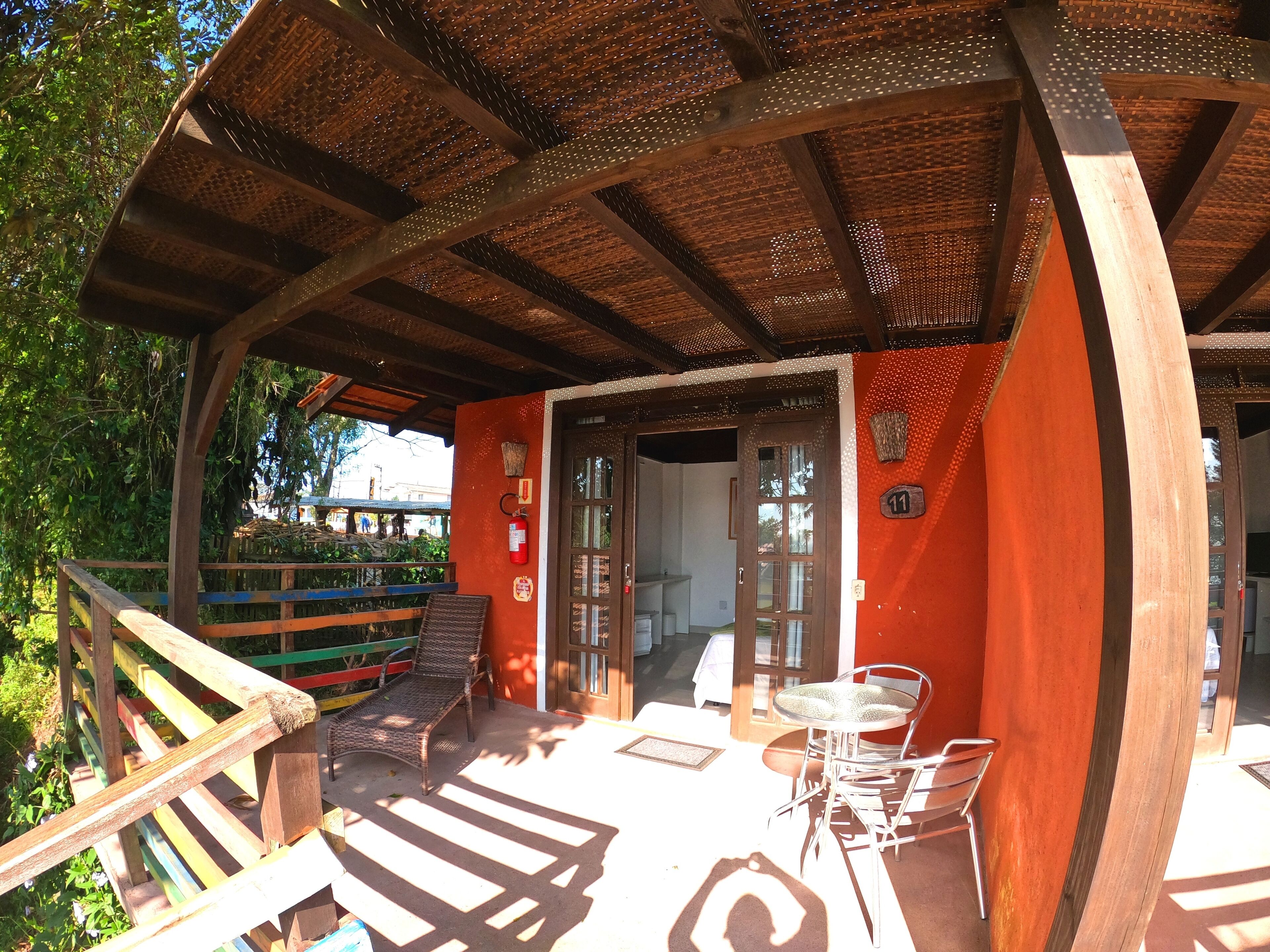 A covered outdoor seating area with wooden furniture and a red wall.