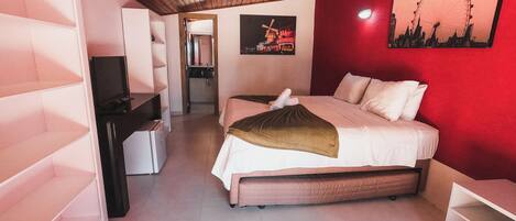 Un dormitorio con una cama, un escritorio, una silla, un espejo y una pared roja con un cuadro.