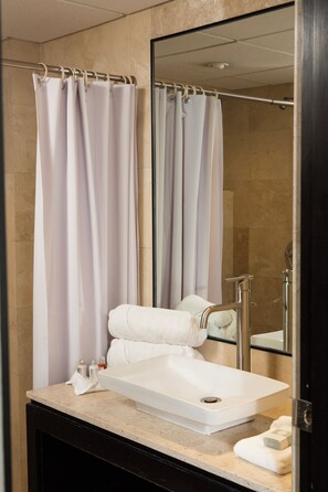 Un baño con lavamanos blanco, toallero, espejo y cortina de ducha.