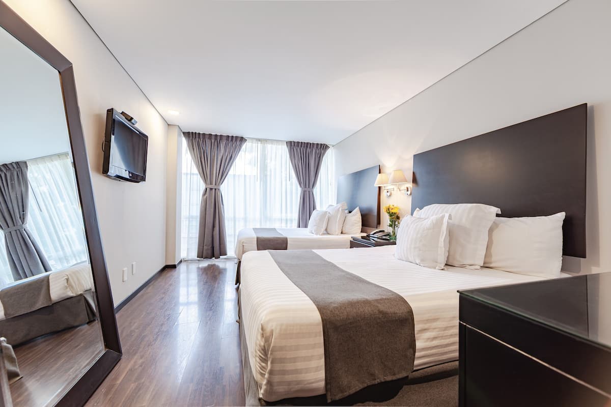 Una habitación de hotel con dos camas, televisión, escritorio y un espejo grande.