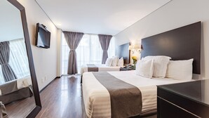 Una habitación de hotel con dos camas, televisión, escritorio y un espejo grande.