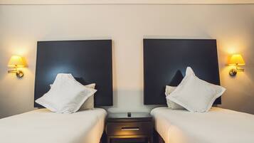 Habitación de hotel con dos camas, cada una con almohada blanca y una mesita de noche entre ellas.