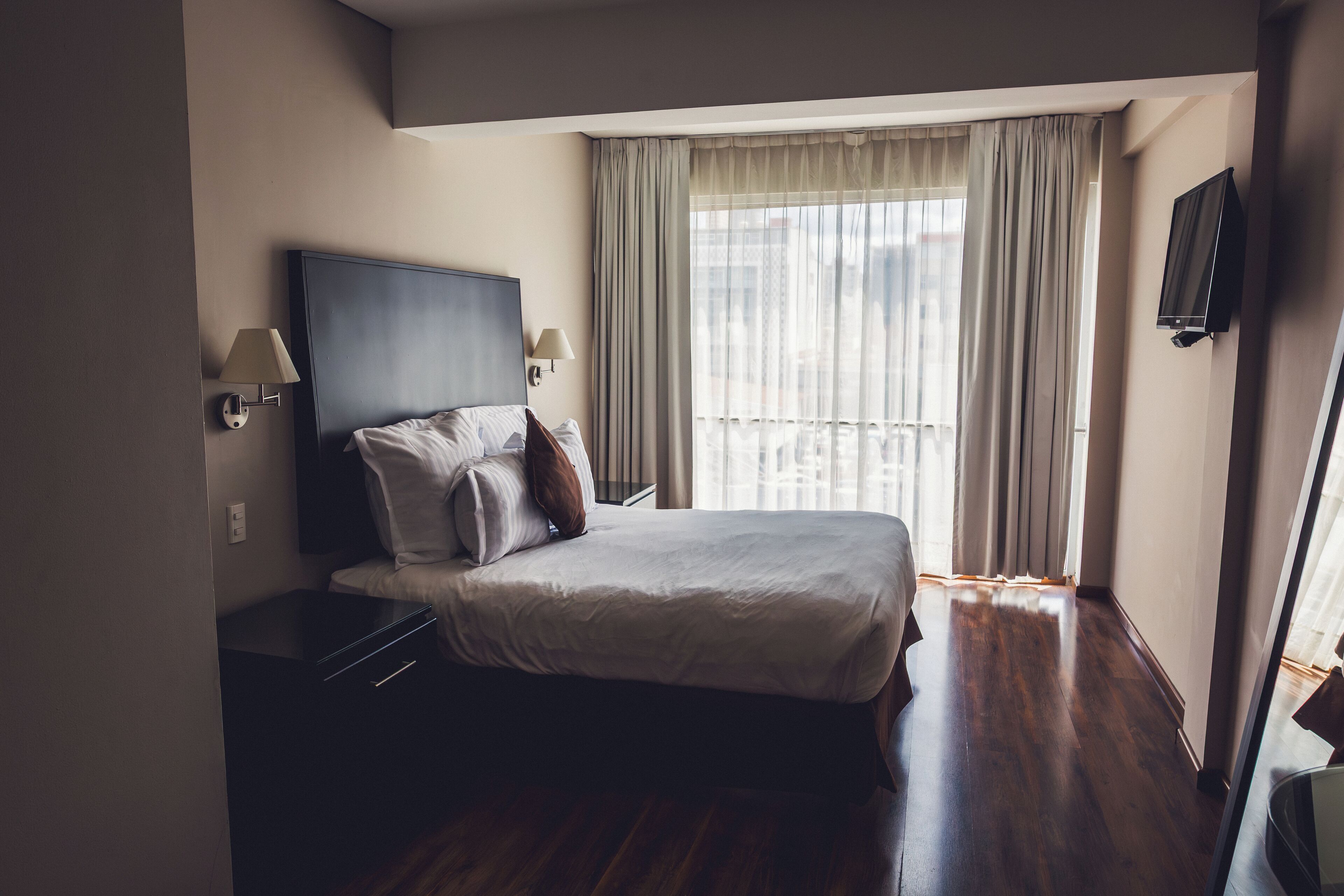 Habitación de hotel con cama, mesita de noche, televisión y ventana con cortinas.