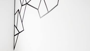 Un dormitorio moderno con una obra de arte geométrica en la pared, una mesita de noche con un jarrón de flores y almohadas a rayas sobre una cama blanca.