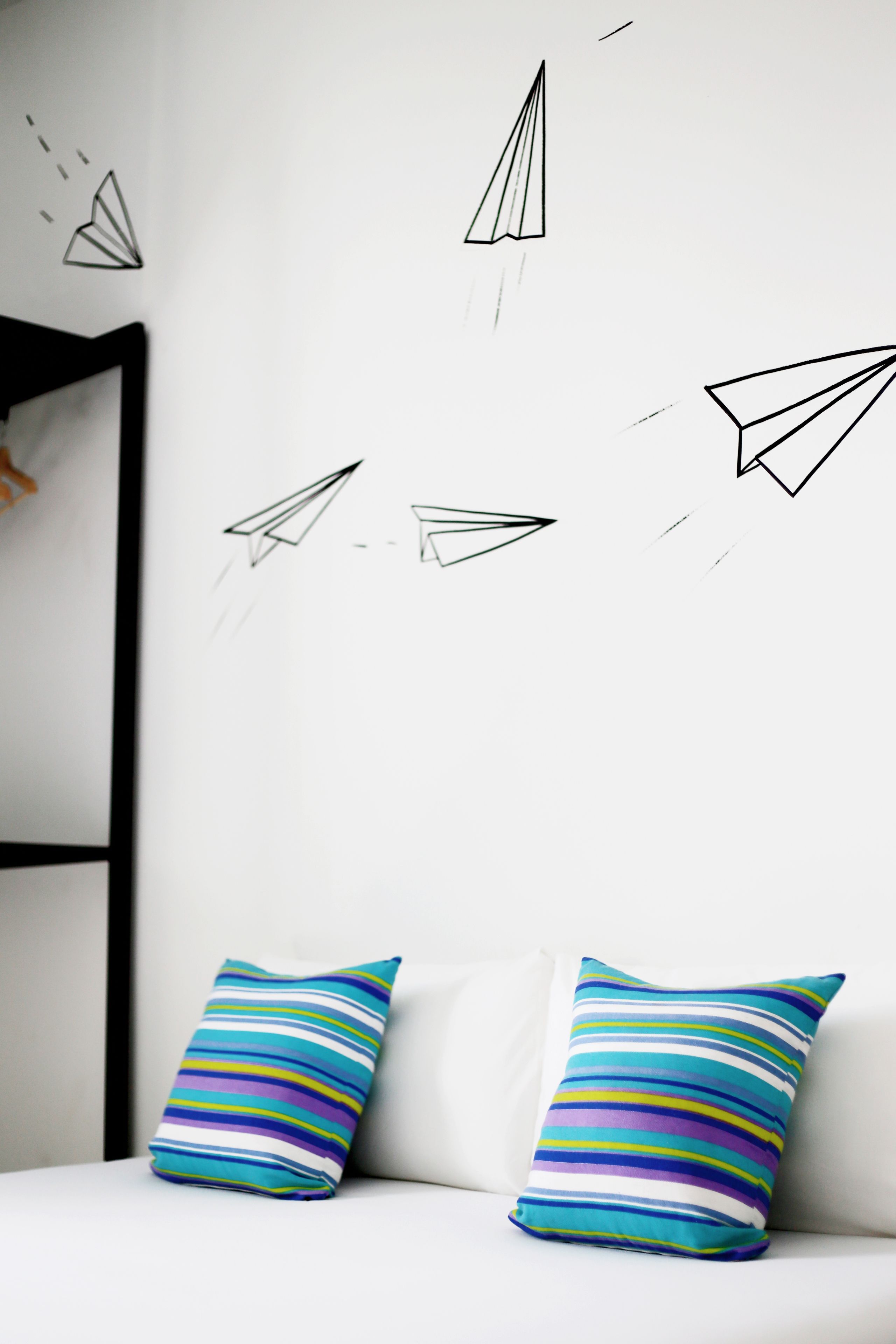 A white sofa with two striped pillows and a wall with paper airplane decals.