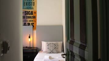 Un dormitorio con cama, mesita de noche, lámpara y una pared con un letrero.
