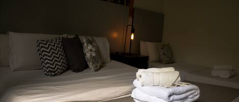 A neatly made bed with white linens and a stack of folded towels.