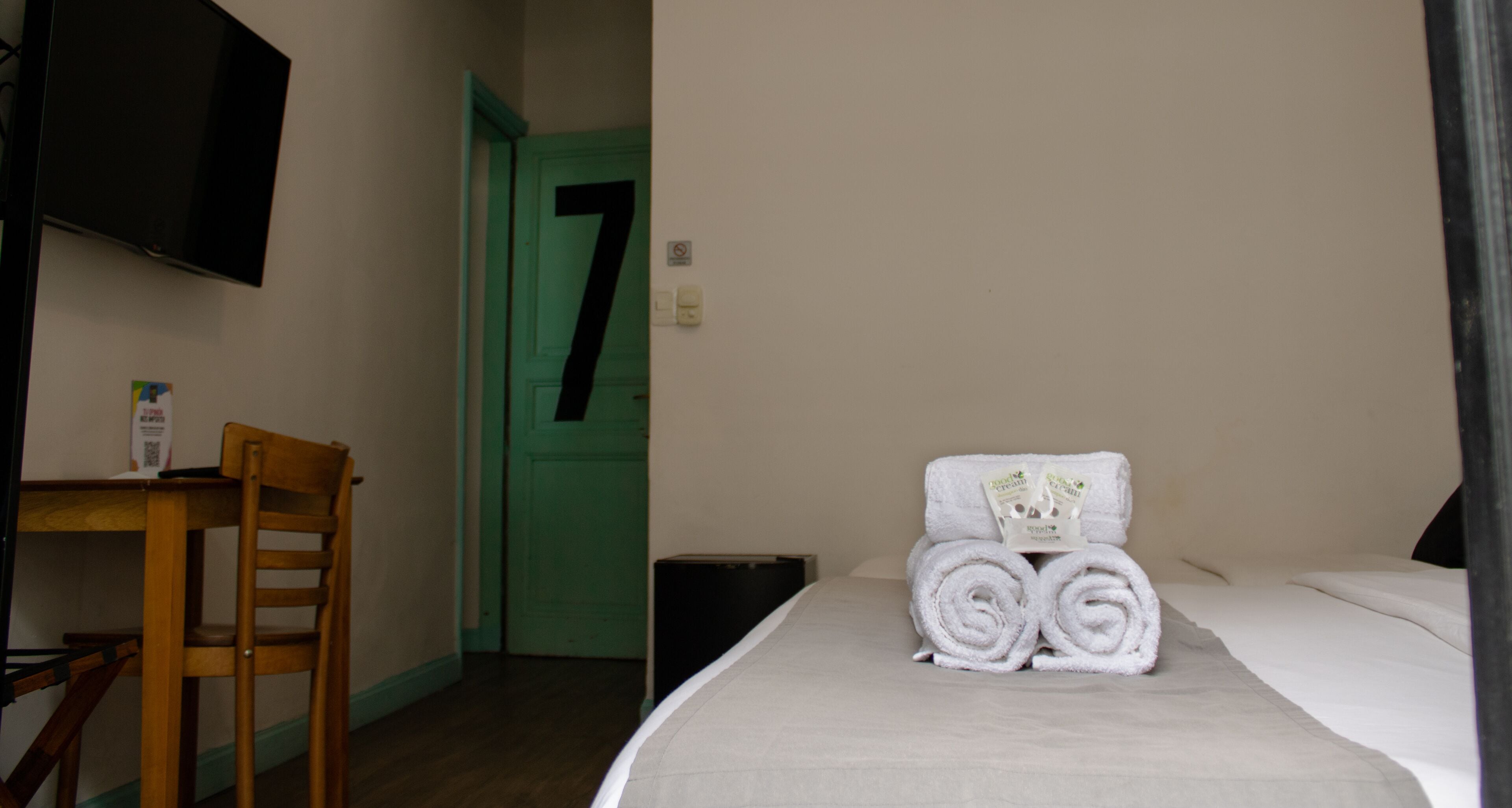 Habitación de hotel con cama, una silla, un escritorio, televisor montado en la pared y una puerta verde con el número 7.