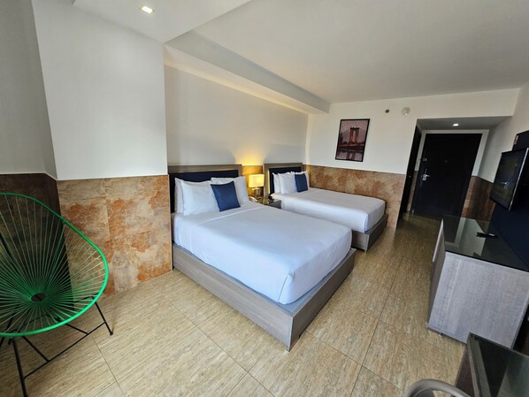 A hotel room with two beds, a green chair, a desk, and a door.