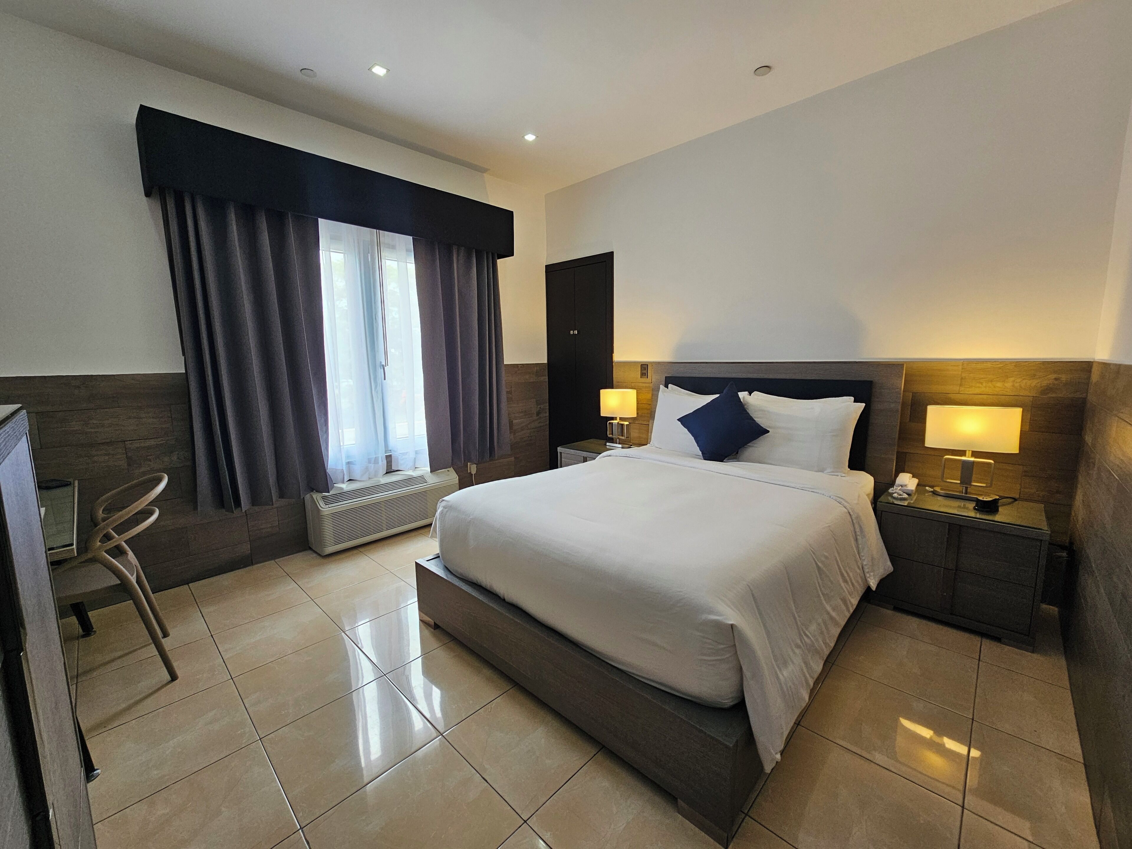 Une chambre d’hôtel avec un grand lit, un bureau, une chaise, un radiateur et une fenêtre avec des rideaux.