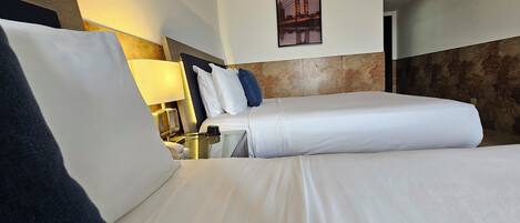 A hotel room with two beds, a nightstand, a lamp, and a framed picture on the wall.