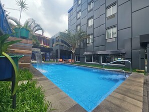 En swimmingpool med et vandfald, omgivet af en moderne bygning med store vinduer og en palme.