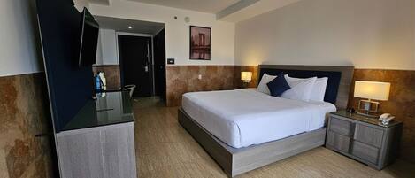 Habitación de hotel con cama, escritorio, silla, mesita de noche y televisor instalado en la pared.