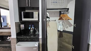 Une petite cuisine équipée d’un four à micro-ondes, d’un réfrigérateur et d’une machine à café. Une porte donne accès à une buanderie avec un lave-linge et un étendoir.