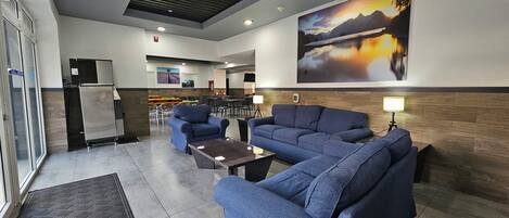 A modern lobby with blue sofas, a coffee table, and a large painting of a mountain landscape.