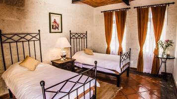 Una habitación con dos camas, una mesita de noche con una lámpara, una pequeña mesa con una vela y un cuadro en la pared.