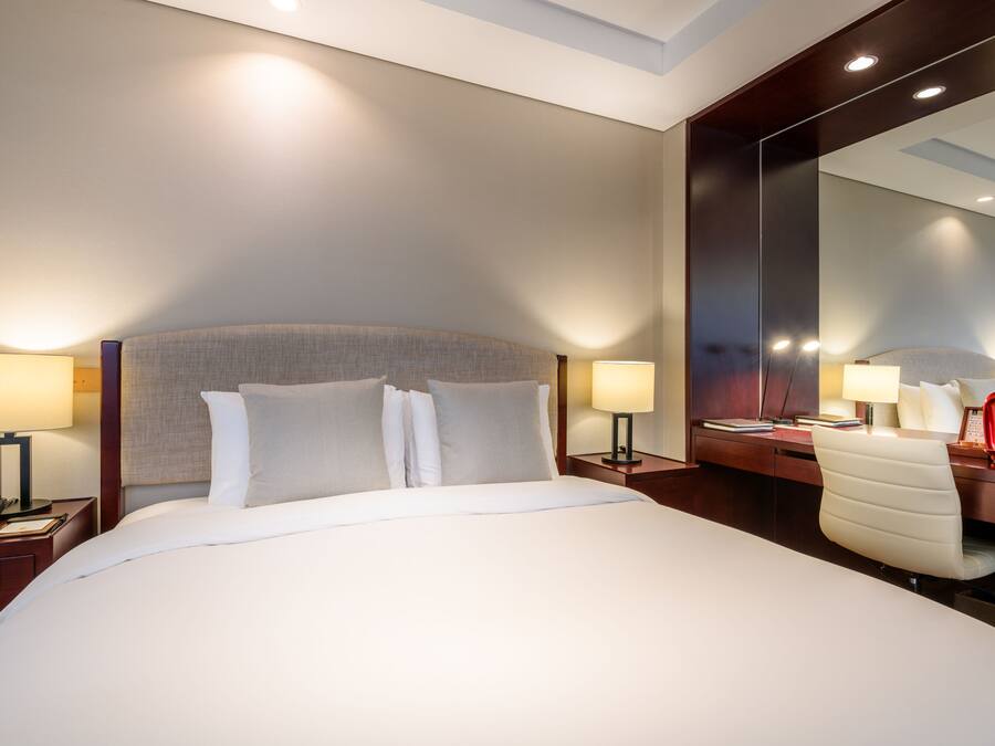 Habitación de hotel con una cama grande, mesitas de noche con lámparas, un escritorio con silla y un espejo amplio.
