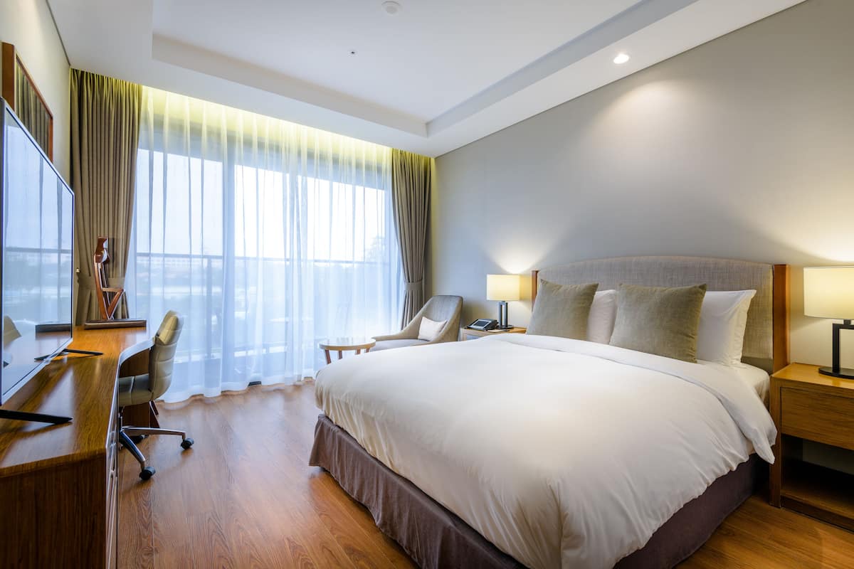 Een hotelkamer met een groot bed, een bureau met stoel, een televisie en een raam met gordijnen.
