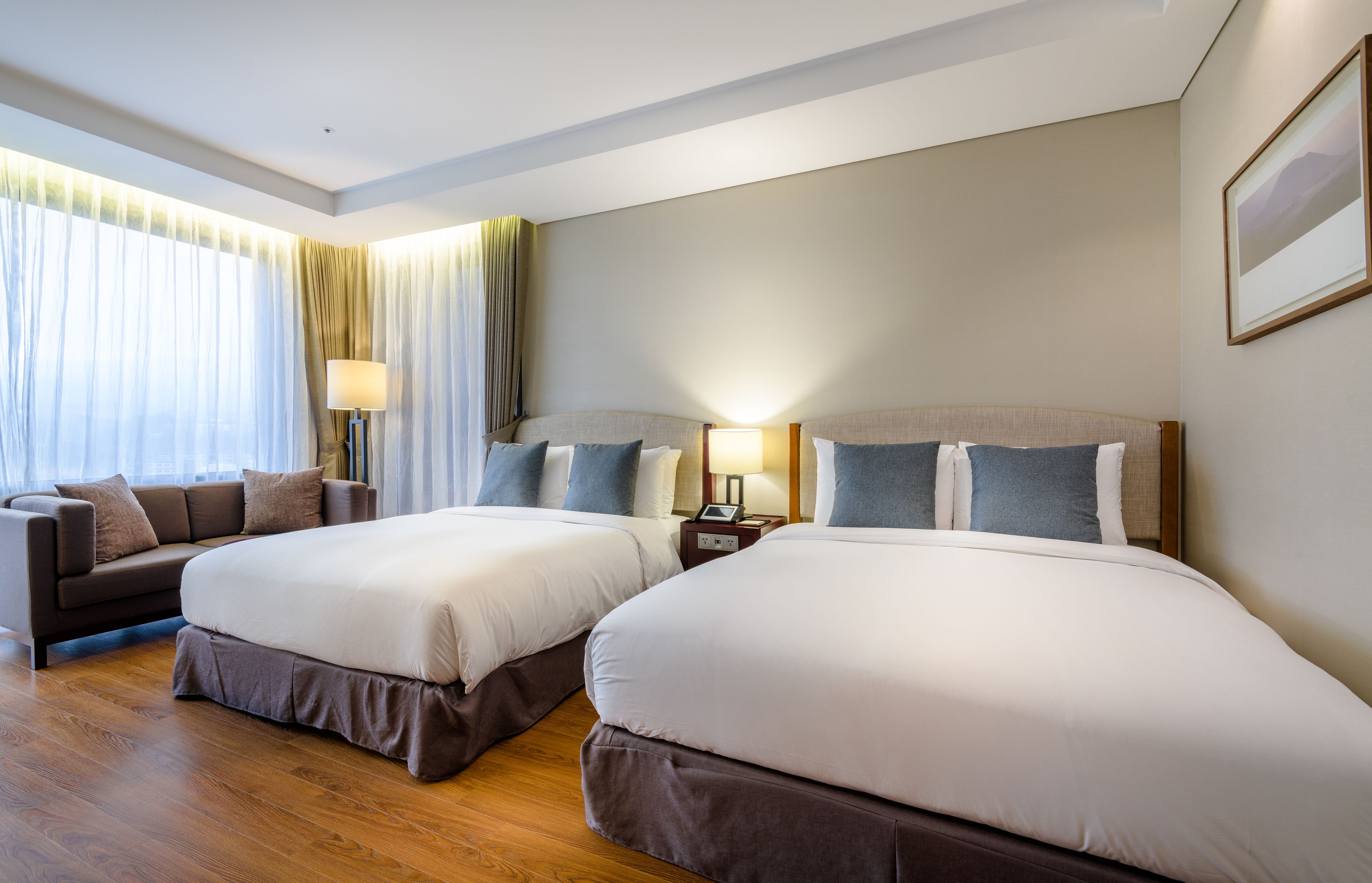 A hotel room with two beds, a sofa, a lamp, and a window with curtains.