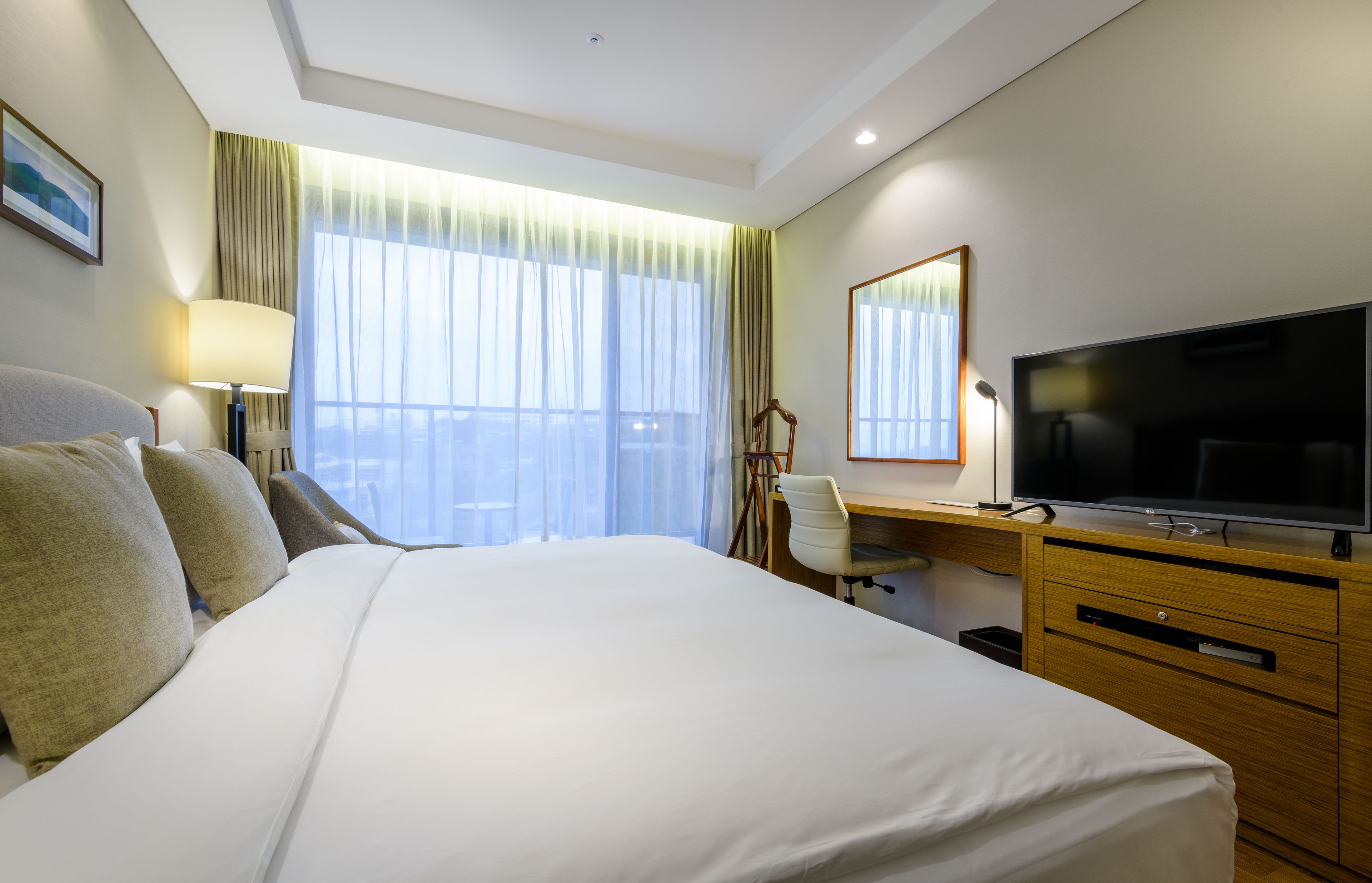 A hotel room with a large bed, a desk with a television, a chair, and a window with curtains.
