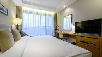 A hotel room with a large bed, a desk with a television, a chair, and a window with curtains.