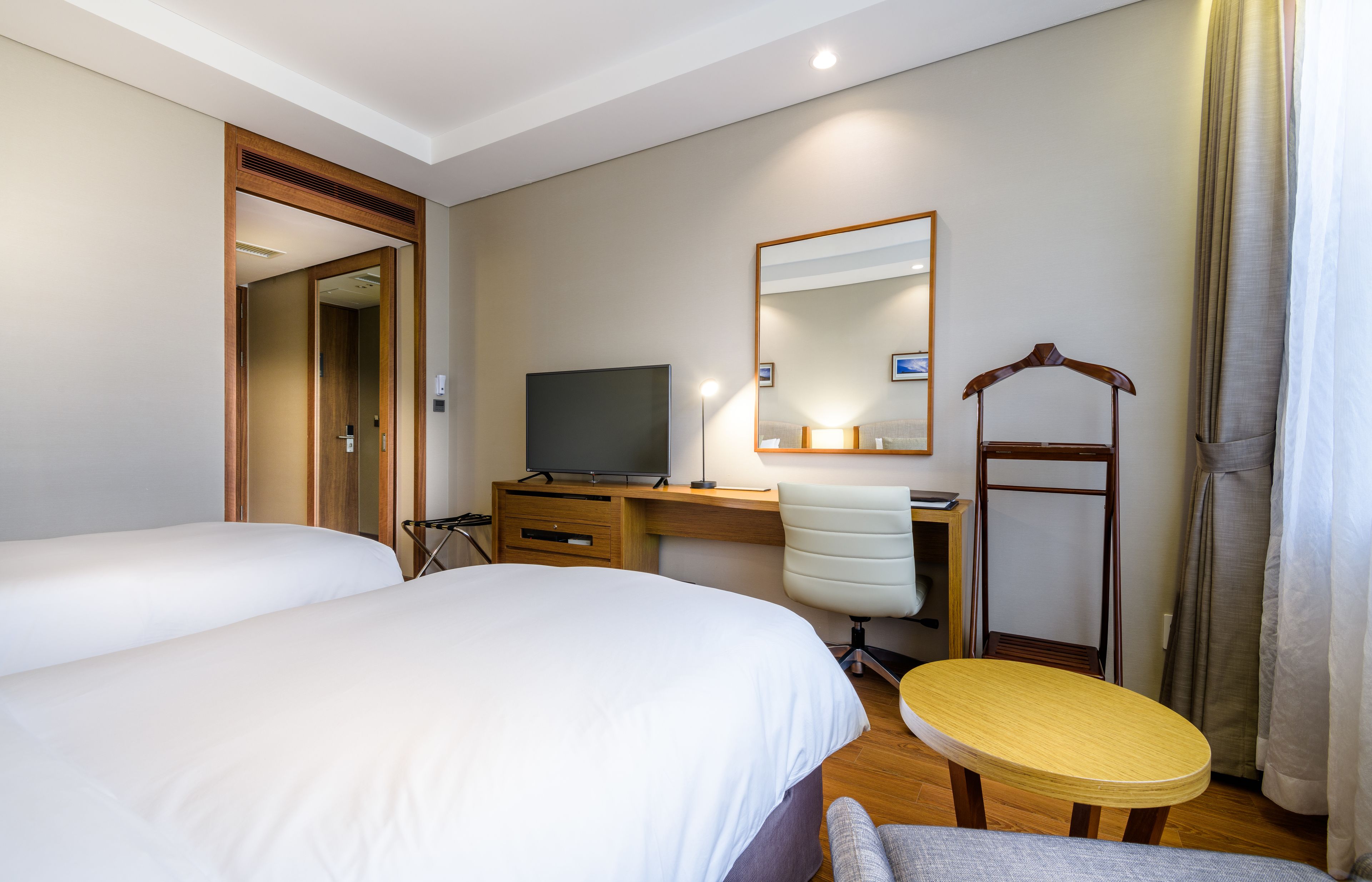 A hotel room with two beds, a desk with a computer, a TV, a chair, a small table, and a mirror.
