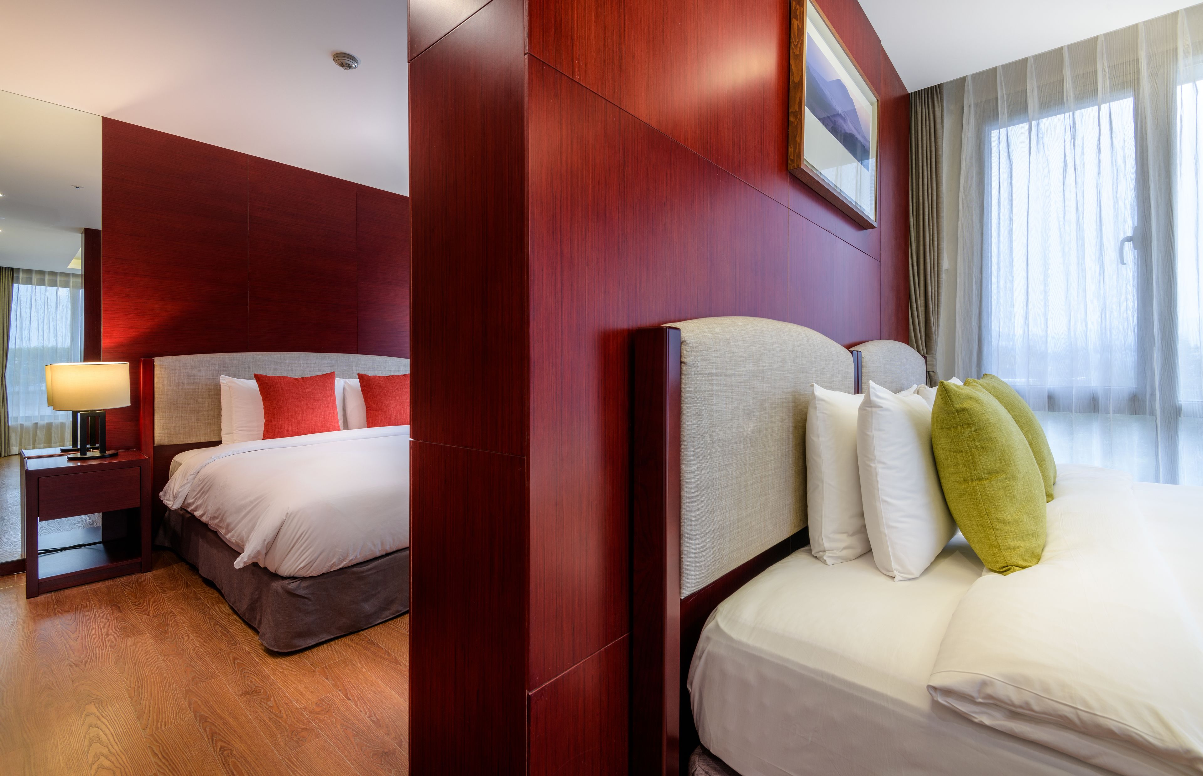 A hotel room with a large bed, a nightstand with a lamp, and a view of the outdoors through sheer curtains.