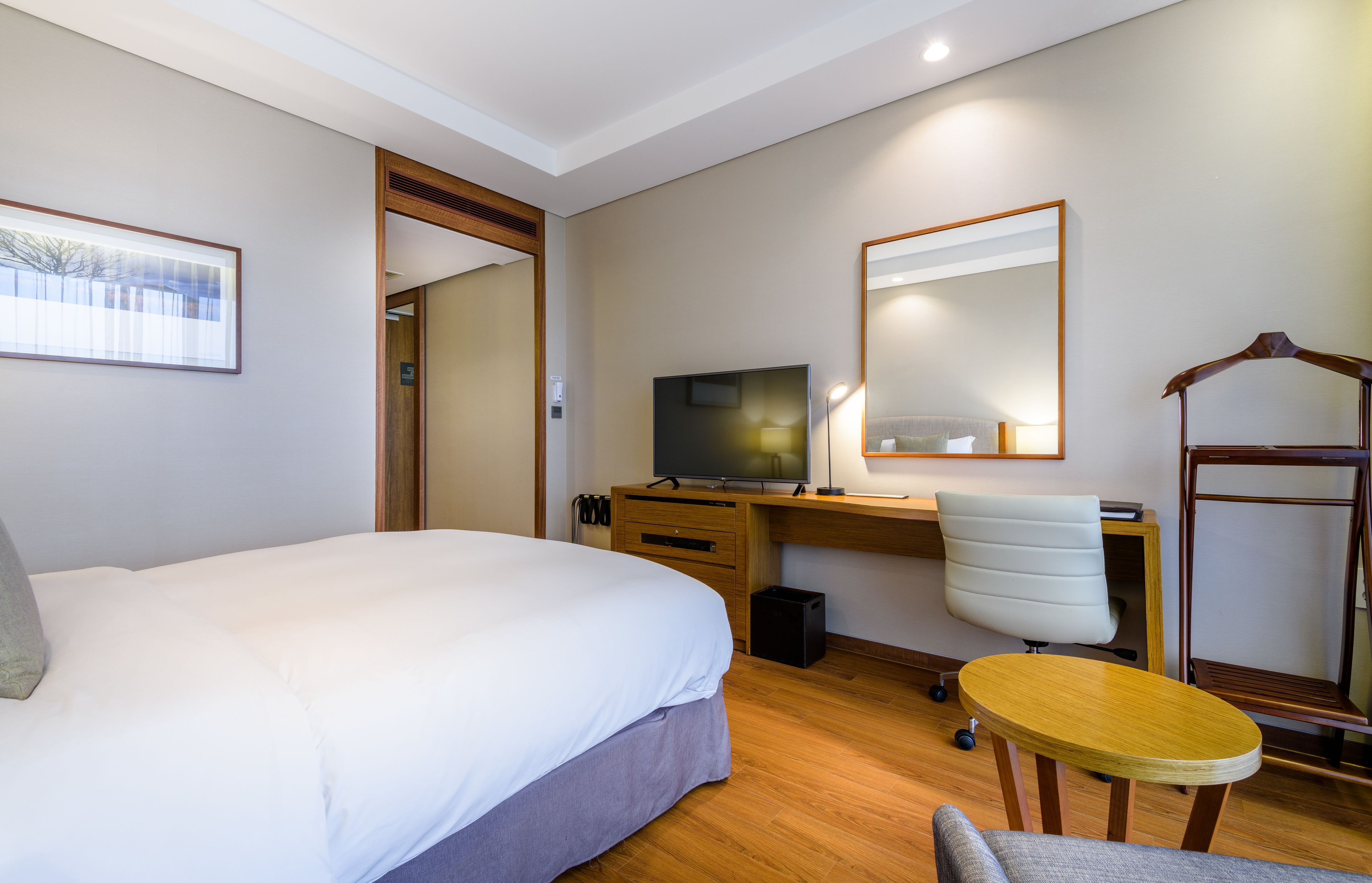 A hotel room with a bed, a desk with a computer, a chair, a small table, and a mirror.