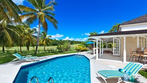 A rectangular swimming pool with two ladders, surrounded by lounge chairs and a covered patio area. - Coconut Grove 1 by Island Villas (Westmoreland)