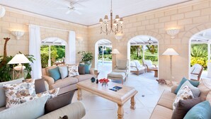 A spacious living room with a beige sofa, a coffee table, and a view of a pool and garden through an arched doorway. - Coconut Grove 1 by Island Villas (Westmoreland)
