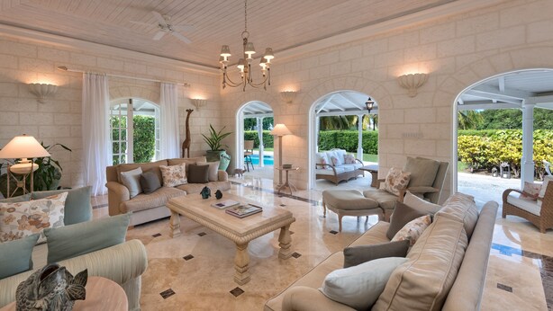 A spacious living room with a large sofa, armchairs, a coffee table, and a chandelier. There are multiple windows and a view of the outdoors. - Coconut Grove 1 by Island Villas (Westmoreland)