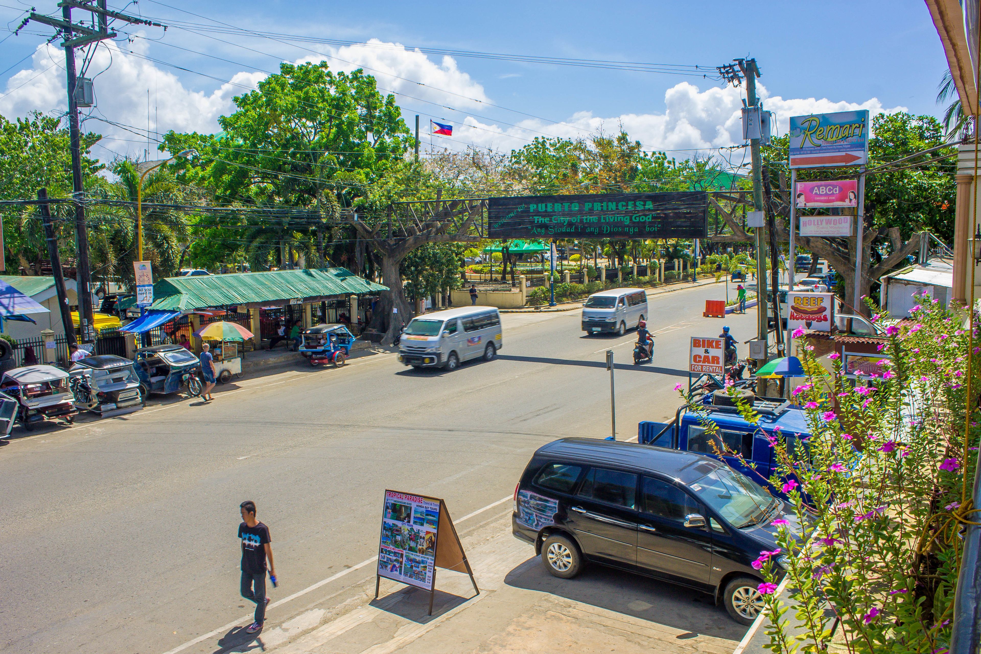 A street view with a sign for 'Puerto Princesa' and various shops and vehicles.