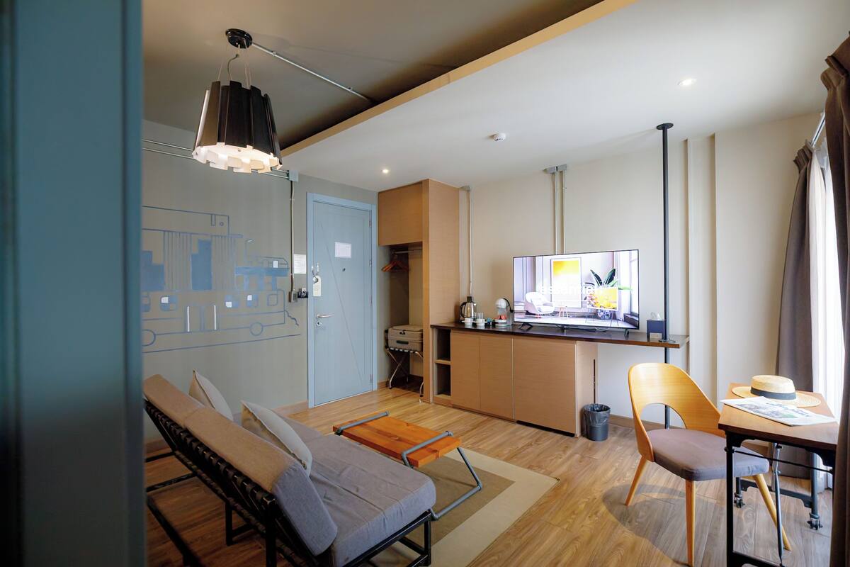 A modern living room with a sofa, a dining table with a chair, a television, and a kitchen area.