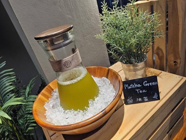 A Matcha Green Tea setup with a glass container on ice, a wooden bowl, and a sign with the tea's name. - THA City Loft by TH District (Bangkok)