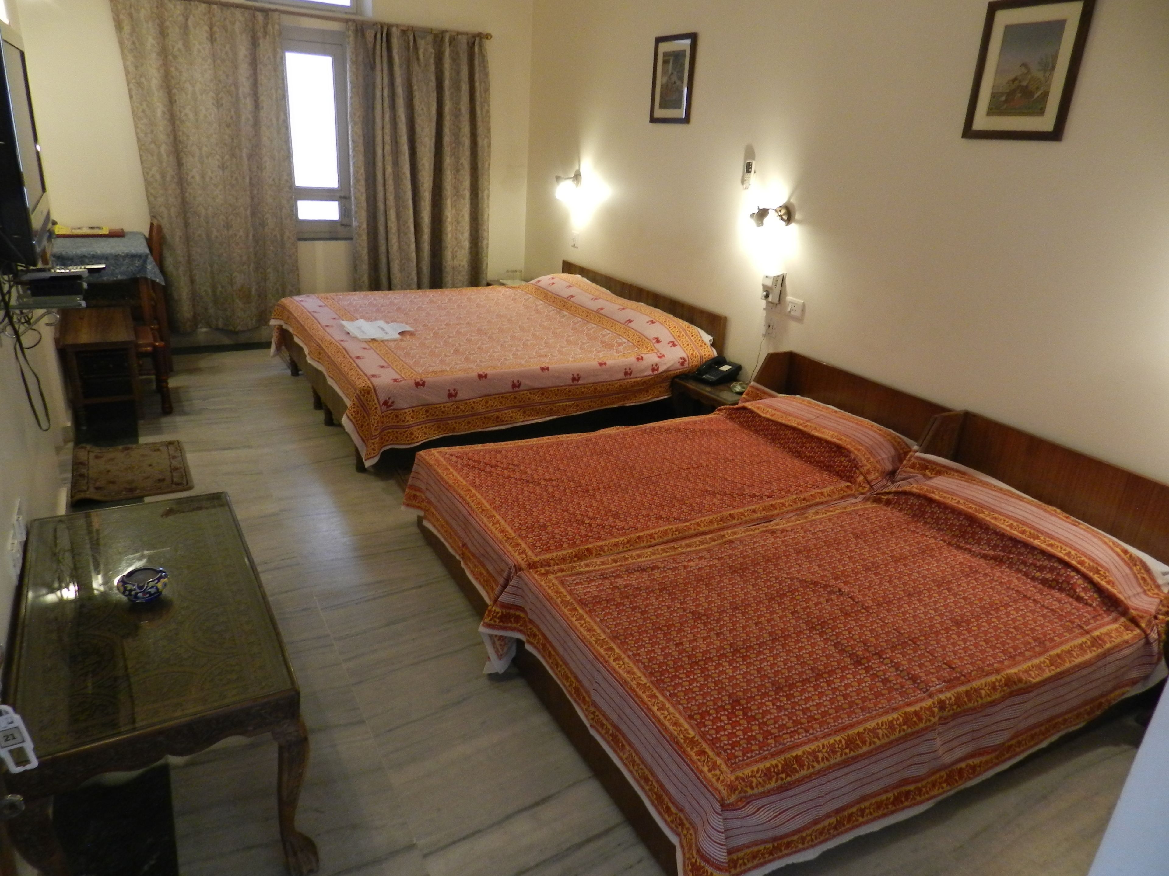 Camera d'albergo con due letti, una scrivania, una sedia e un piccolo tavolo.