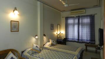 Habitación de hotel con dos camas, un escritorio, una silla, un ventilador de techo y una ventana con cortinas.