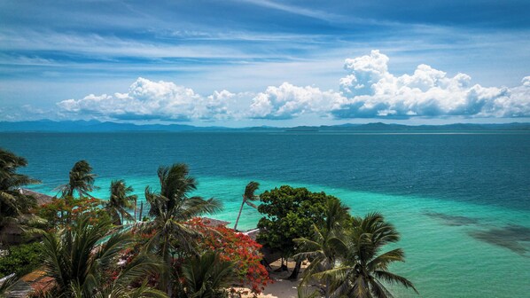 Ein tropischer Strand mit klarem türkisblauem Wasser, Palmen und Blick auf entfernte Berge.